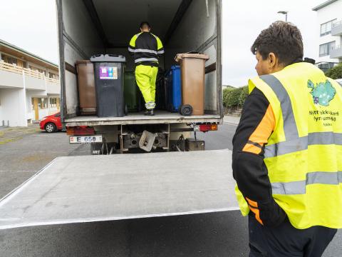 Truck with waste bins and people working on the bin swap.