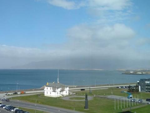 Höfði, loftmynd eða tekin úr hárri byggingu. Horft út á sjá í átt að Esju, blár himinn en mikið mengunarský, líklega vegna sandfoks.