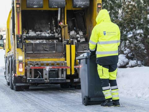 Waste collection worker in yellow overalls next to a bin and waste collection vehicle.