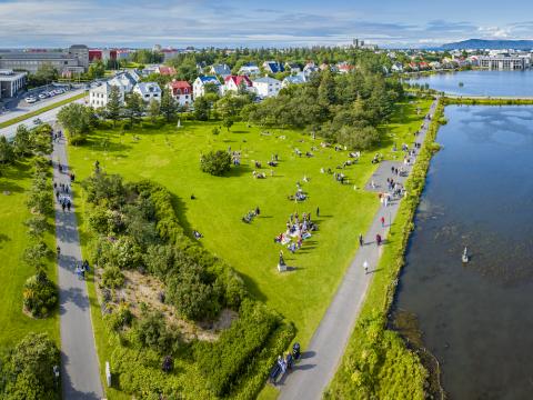 Overview image showing grass, trees, streets, a pond and people.