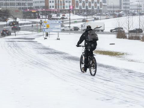 A cyclist on a snow-covered road with buildings nearby.