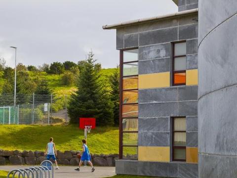 Mynd af húsaskóla. Tvö börn spila körfubolta á leikvelli.