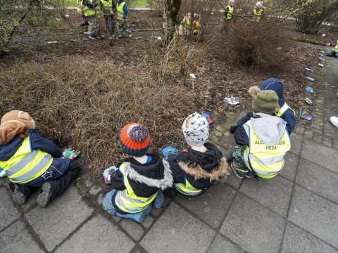Preschool children seen from behind crouching by a garden bed. 