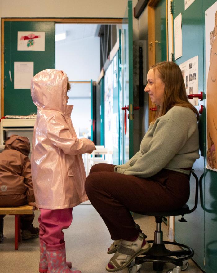 Leikskólakennari og barn í bleikri regnkápu í andyrinu á leikskólanum Ægisborg