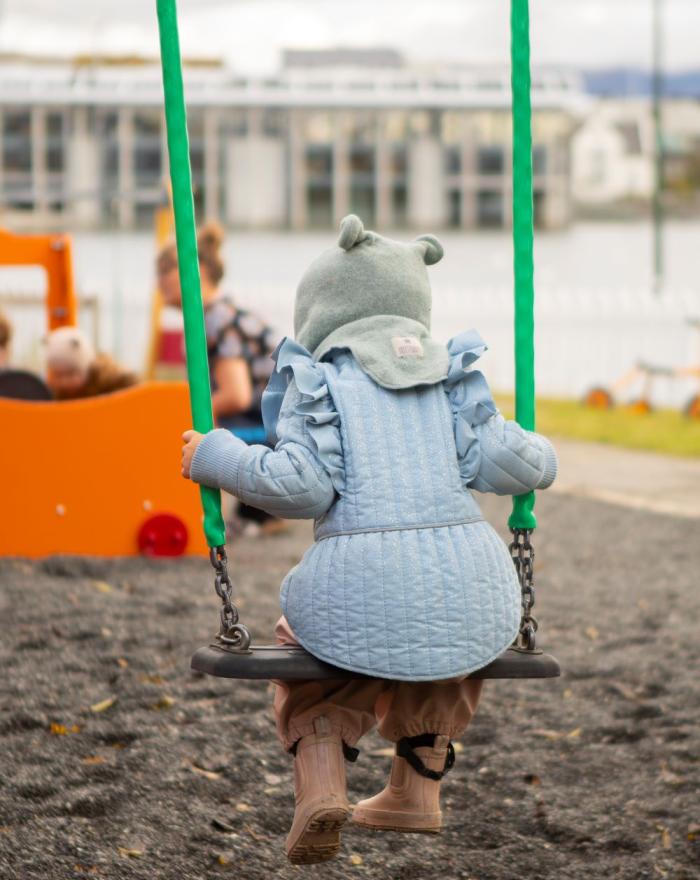 Child in a blue jacket swinging at Tjörn preschool