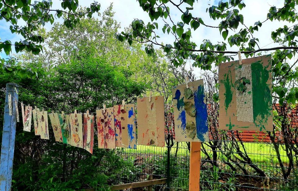 Children's artwork hanging on a line during summer at Lyngheimar preschool's playground.