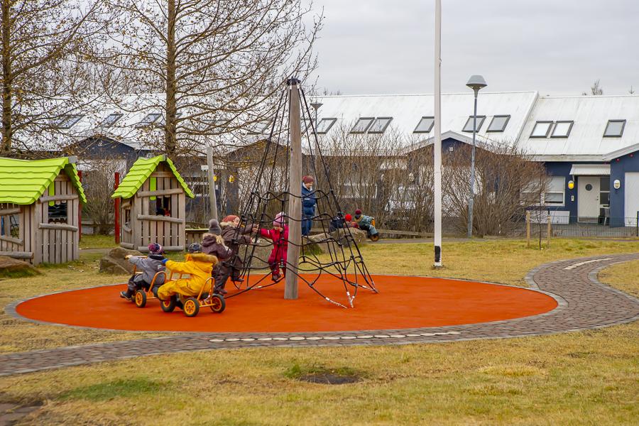 Children playing on the climbing structure and riding tricycles in Lyngheimar's outdoor play area.