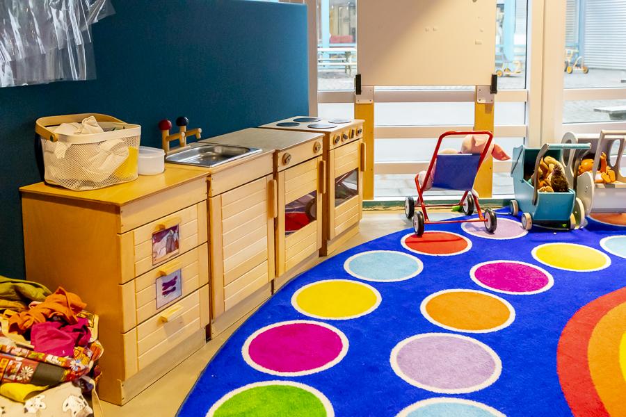 Toy kitchen, large blue rug with colored dots and doll strollers at Lyngheimar preschool.