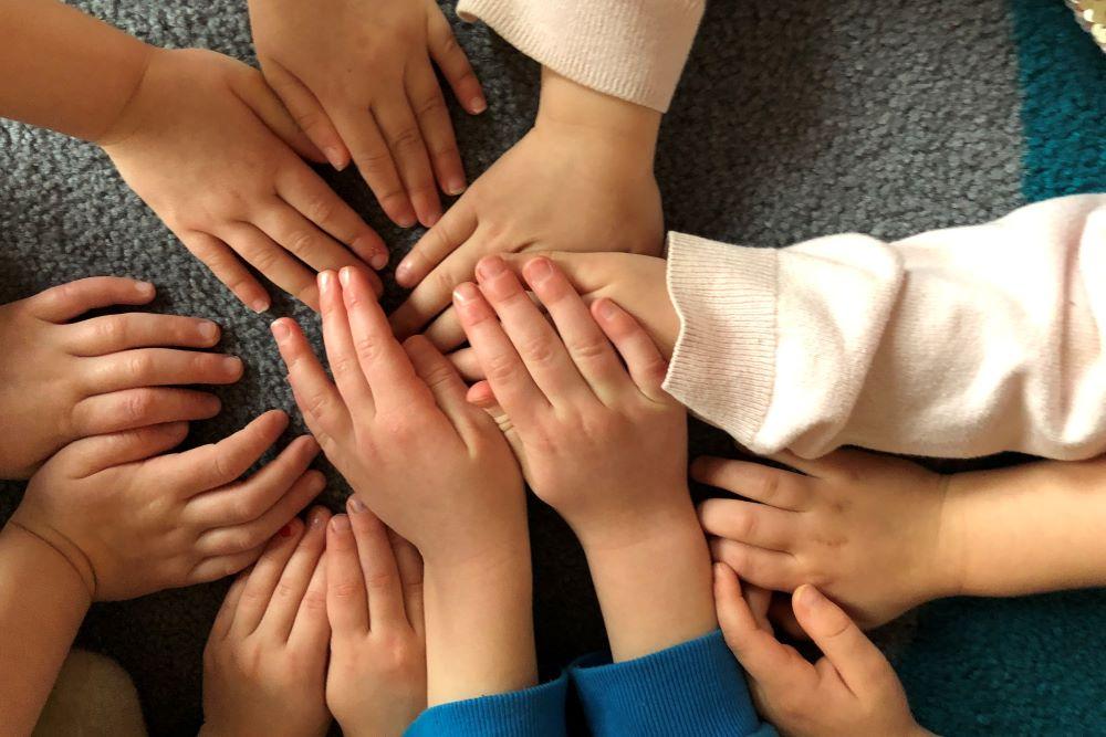 Ten preschool children's hands coming together in the center of the image