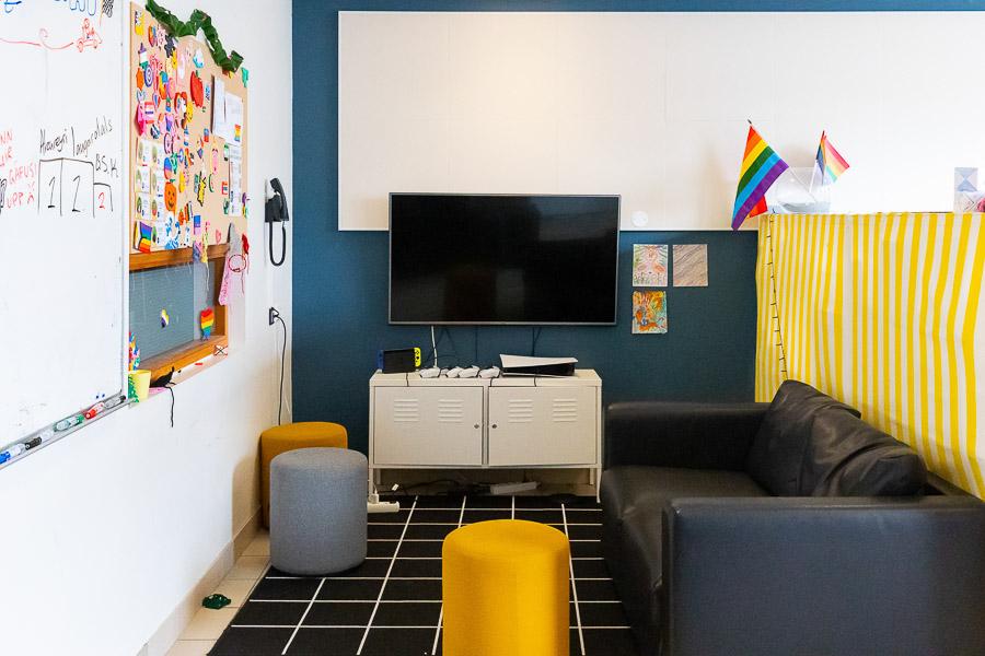 A black couch, a television, and yellow and gray cushions. Whiteboards and pictures. 