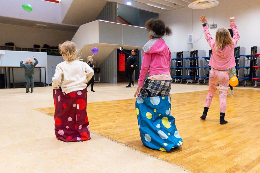 Börn í pokahlaupi og að leika sér að blöðrum í íþróttahúsi. 