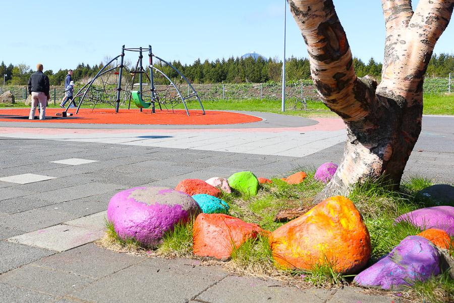 Trjábolur og stórir steinar málaðir með allskonar litum. Klifurgrind í baksýn. 