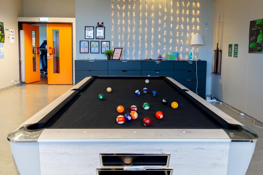 A hall with a pool table and orange doors. 
