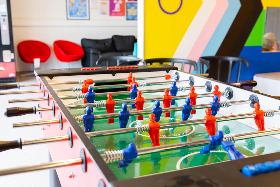 A foosball table in the foreground and red chairs in the background. 