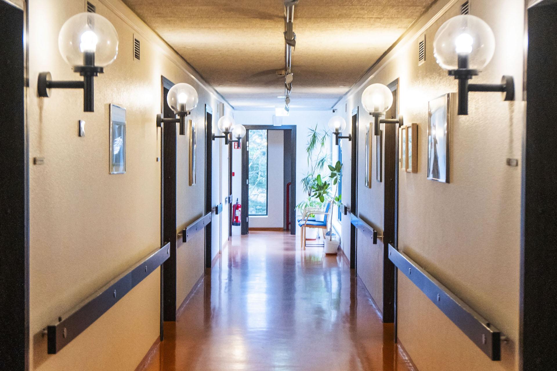 Horft inn eftir gangi, ljóskúplar við hverja hurð á ganginum