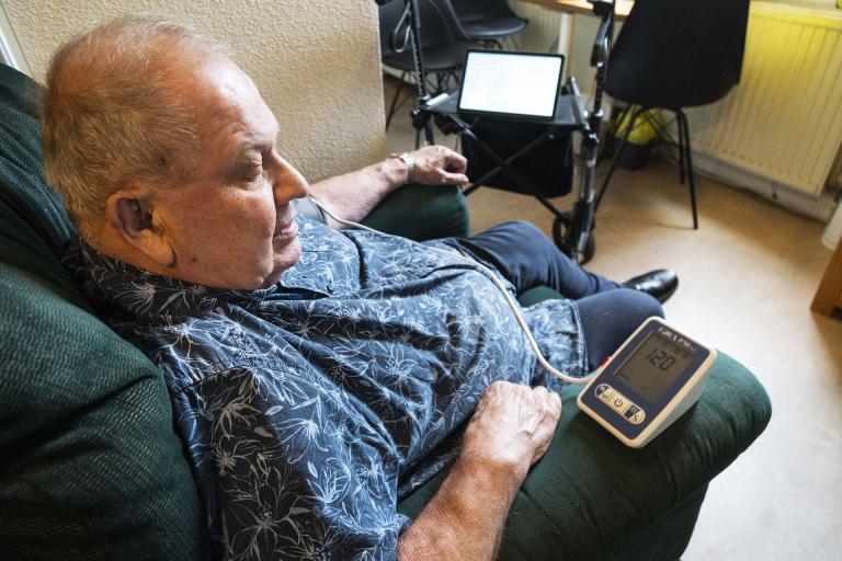 Image taken from behind Pálmi as he measures pressure and looks at the numbers displayed on the blood pressure monitor.