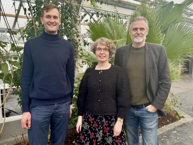 Three people photographed with vegetation in the background.