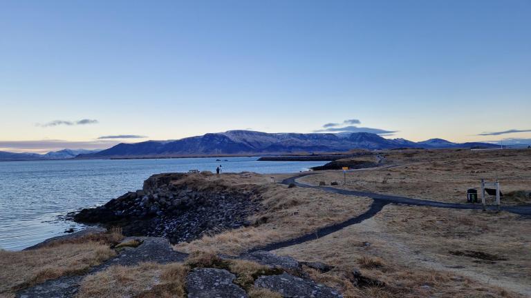 Laugarnestangi, looking over the grassy area and walking path. The sea and mountains in the distance. Cool, clear sky.