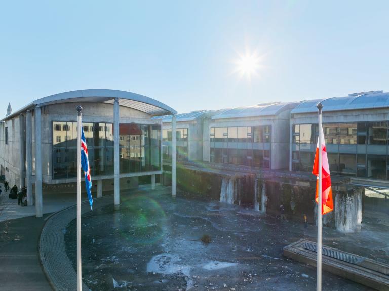Íslenski og grænlenski fáninn við hún á fánastöngum Ráðhússins. Ráðhúsið í bakgrunni, sól á bláum himni. Logn.