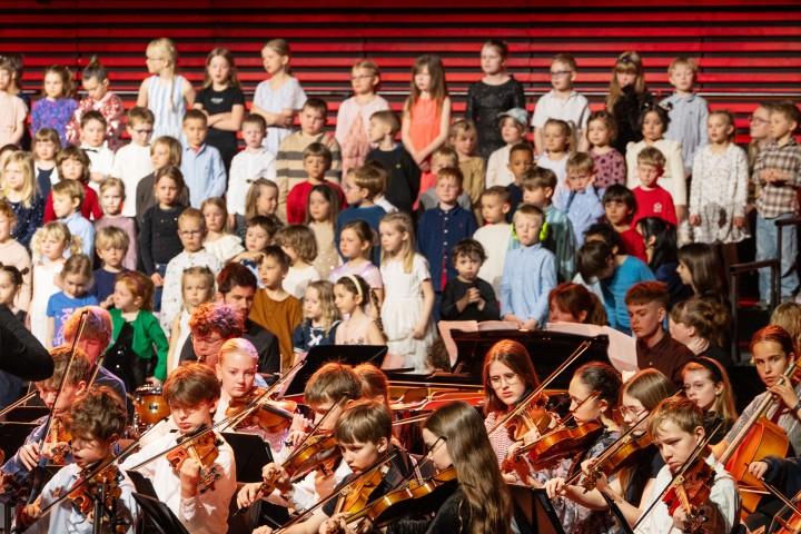 The children sing accompanied by young musicians from the city's music schools.