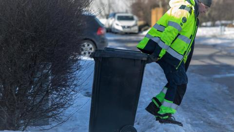Sorphrðumaður að störfum í snjó með gráa tunnu.