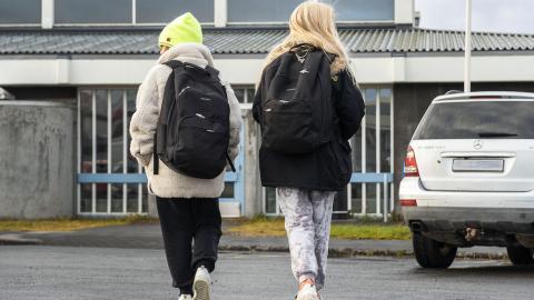 Skólakrakkar að ganga í skólann með skólatöskur á bakinu.