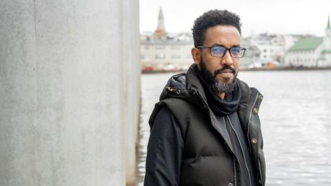 Samson Haileselassie Habte, landflótta blaðamaður frá Erítresu og skjólstæðingur ICORN, stillir sér upp við súlu á Ráðhúsinu. Í bakgrunni er Fríkirkjuvegur og Hallgrímskirkja.