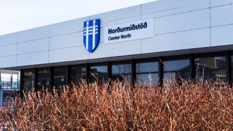 Hvítt hús með brúnum gluggum og runnar i haustlitum í forgrunni. Á húsinu er merki Reykjavíkurborgar og til hliðar stendur Norðurmiðstöð.