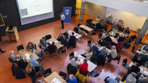 Fólk situr við borð í sal Vogaskóla og borgarstjóri stendur við skjá