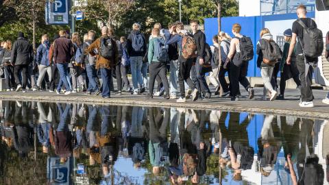Group of adolescents walking along Tjörnin lake, which reflects their image.