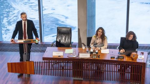 Mayor Einar Þorsteinsson stands at the podium in the City Council chamber. Magnea Gná and Helga Laxdal are seated at a table