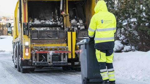 Waste collection worker in yellow overalls next to a bin and waste collection vehicle.