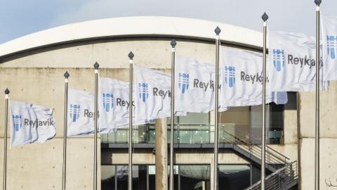 Reykjavík City Hall, with a flag pole stand on the bridge in the foreground, close-up of the city's flags with the building visible in the background