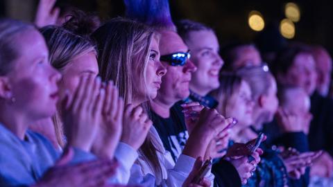 Close-up of people in the front row at a concert. Dark, people of all ages.