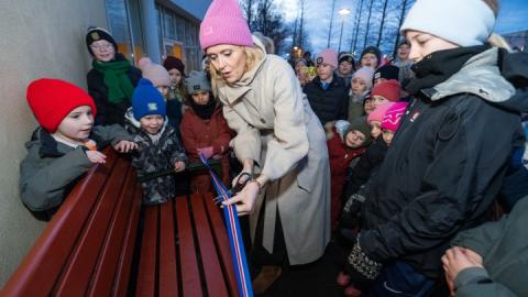 Mayor Heiða Björg Hilmisdóttir dedicates the buddy bench at Engjaskóli by cutting a ribbon as students look on.