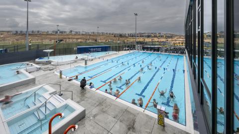 Dalslaug swimming pool, photographed from the building looking down over the pool area. People in the pool. Overcast conditions outside.
