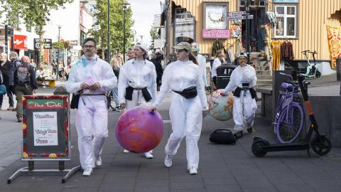 Young people in white overalls carrying a large pink ball walk down Bankastræti. Street art hosted by Hitt Húsið Youth Center.